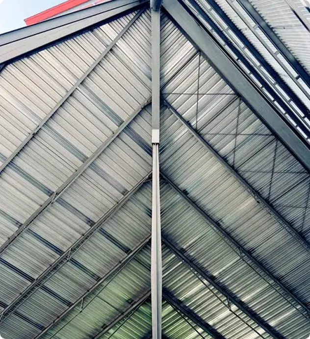 Vista interna de telhado com estrutura metálica industrial cinza e telhas onduladas em formato de arco triangular.